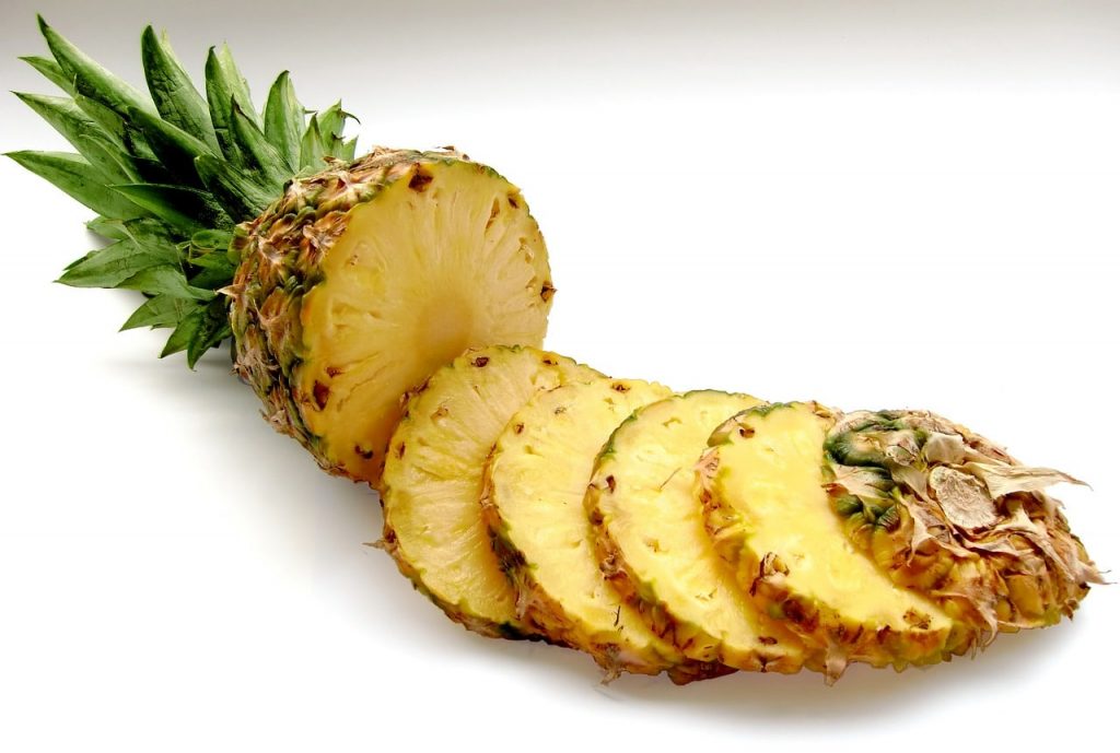 A fresh pineapple with green leaves, sliced into thick, juicy rounds, displayed on a white background.