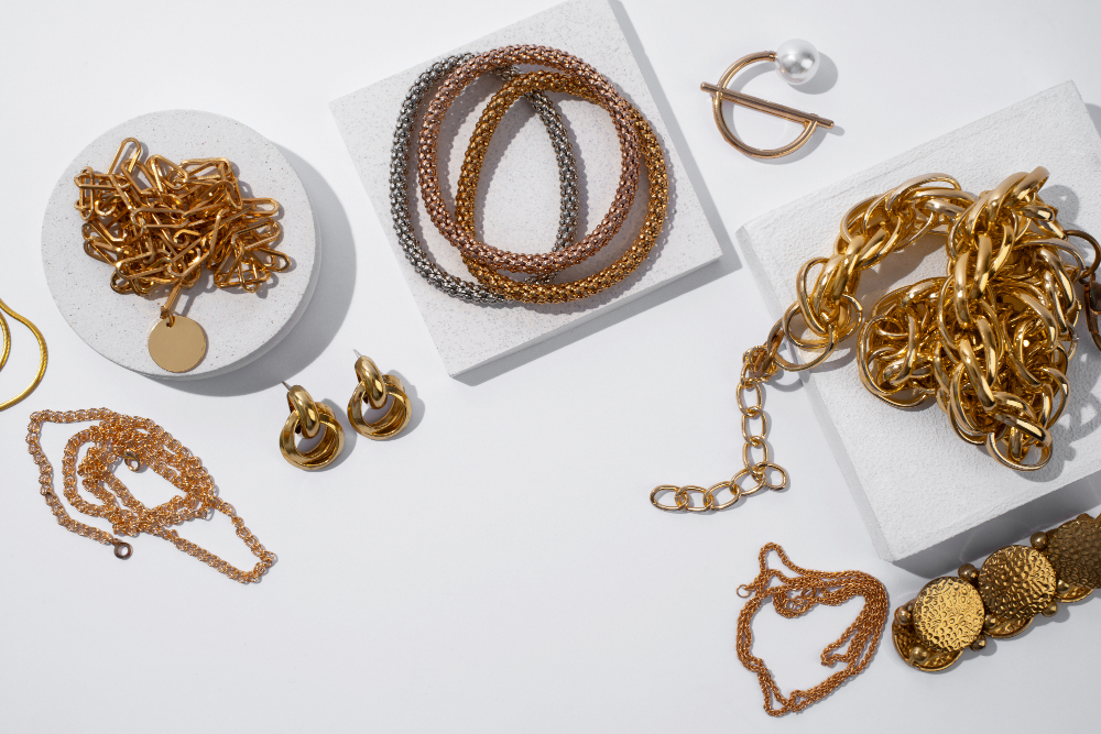 An assortment of copper and gold jewelry pieces displayed on minimalist white blocks, including chains and earrings.